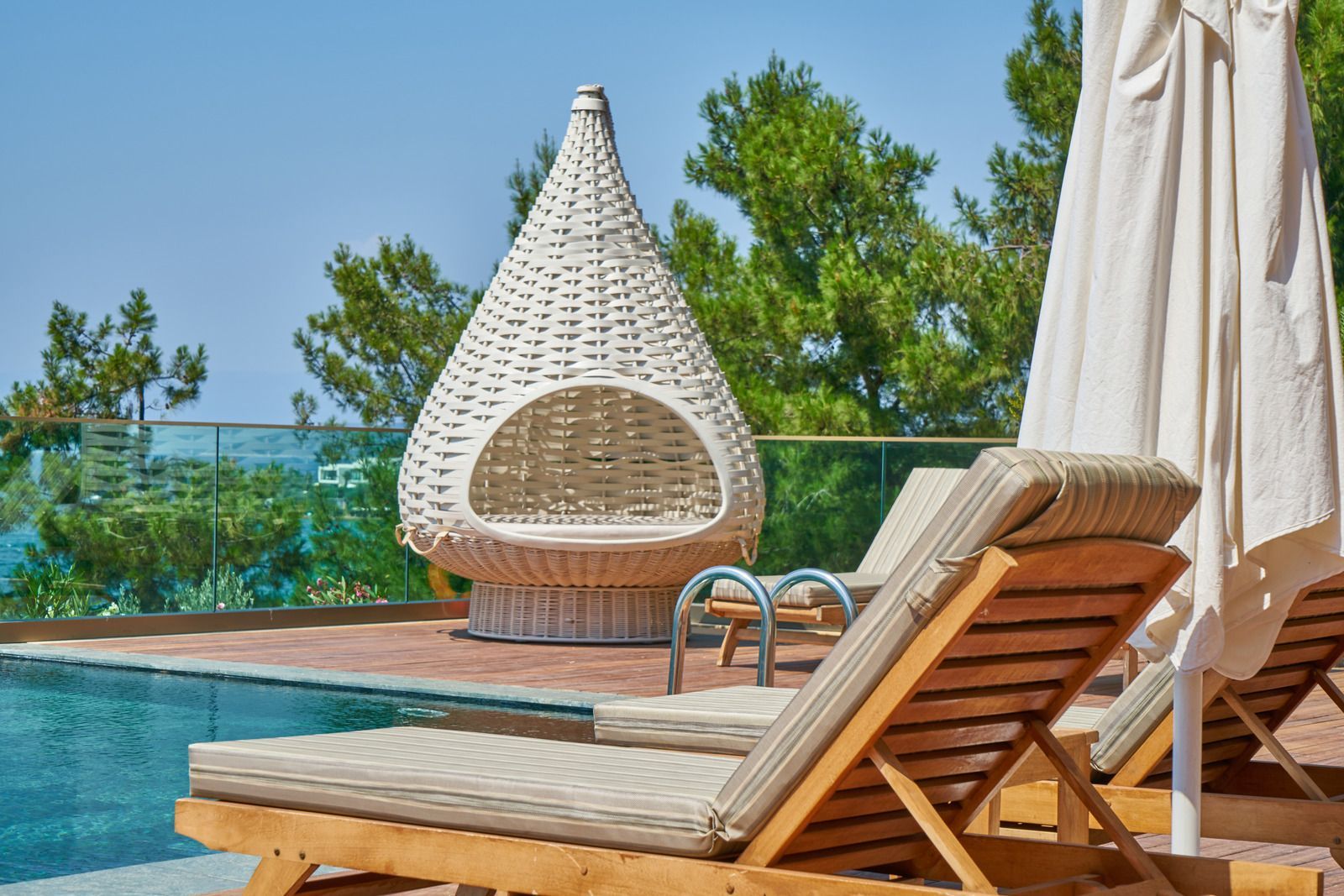 A wicker chair and umbrellas are sitting next to a swimming pool.