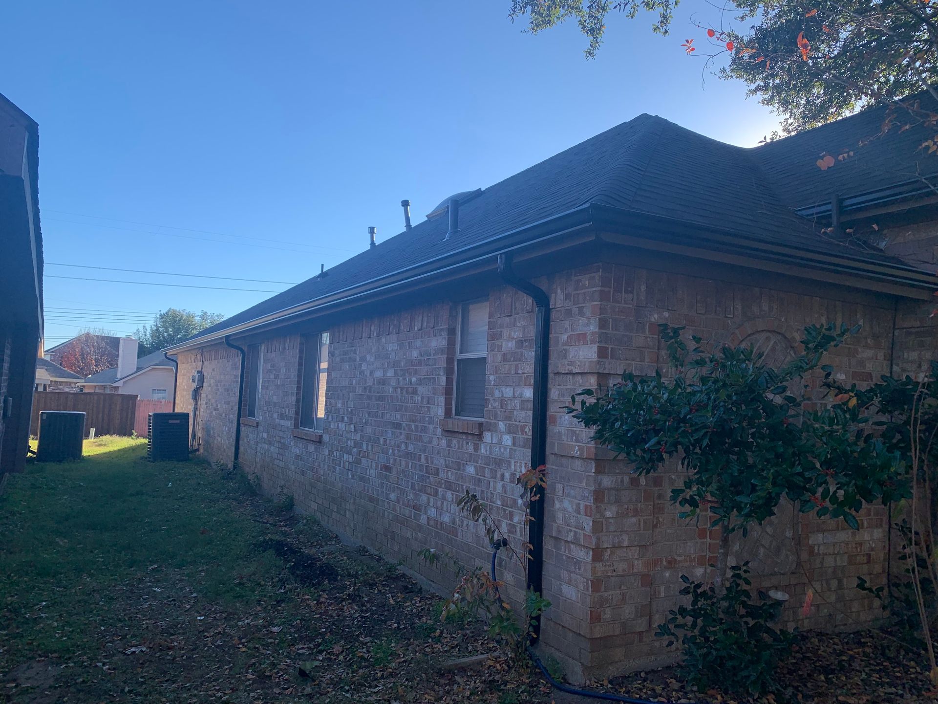 The back of a brick house with a black roof and gutters.