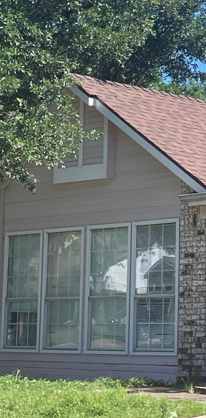 Exterior view of a house with brown roof and four tall windows reflecting the outdoors.