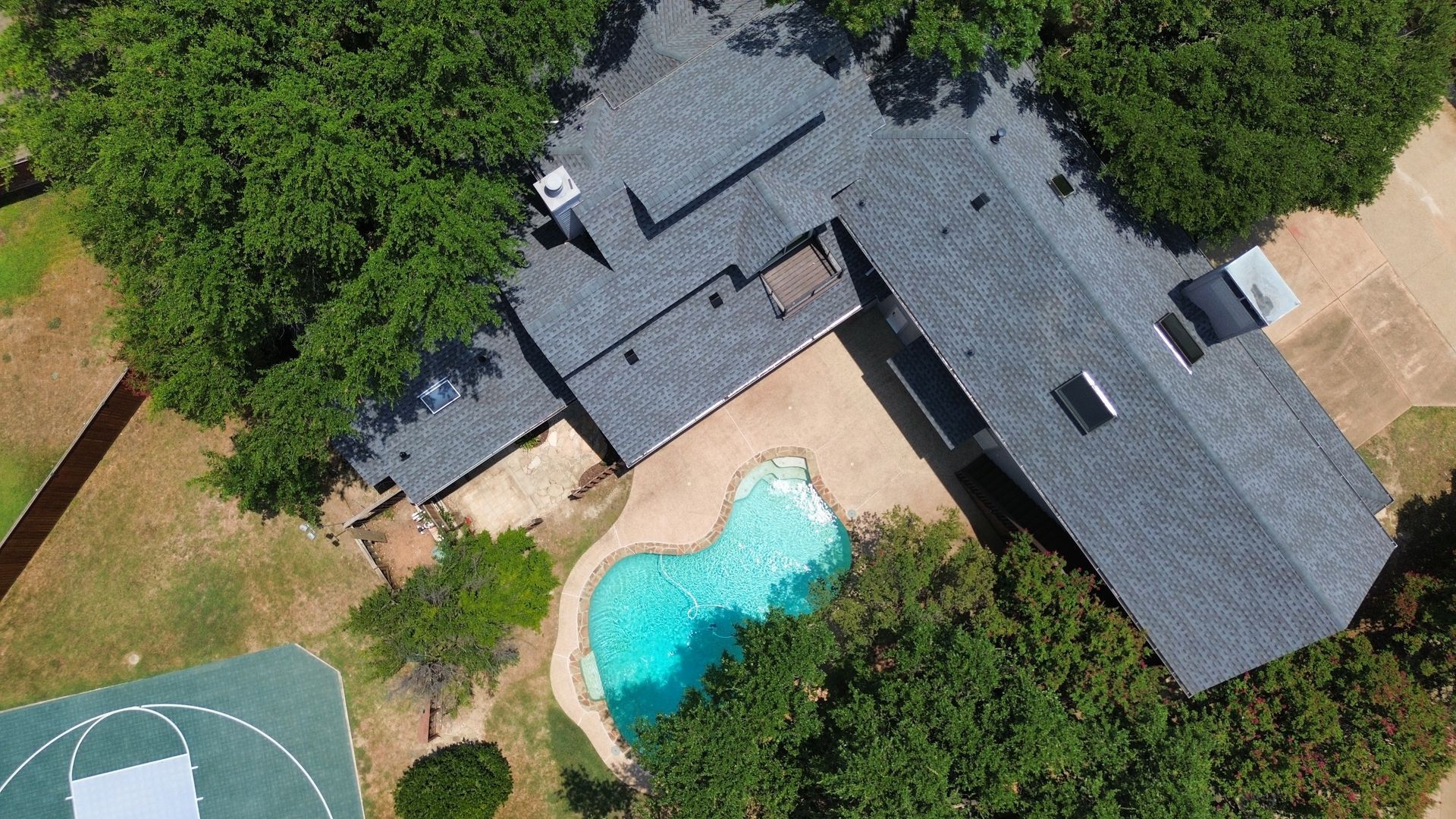 An aerial view of a house with a pool and a basketball court.