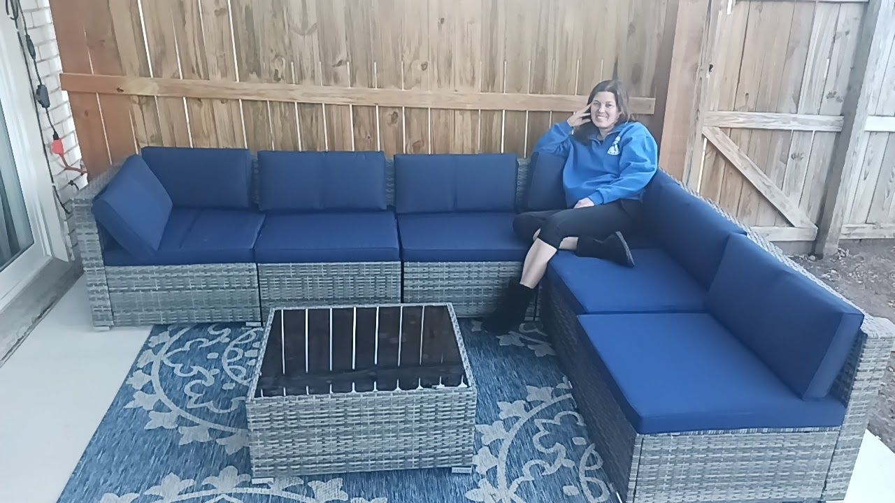 A woman in a blue jacket is sitting on a blue sectional couch.