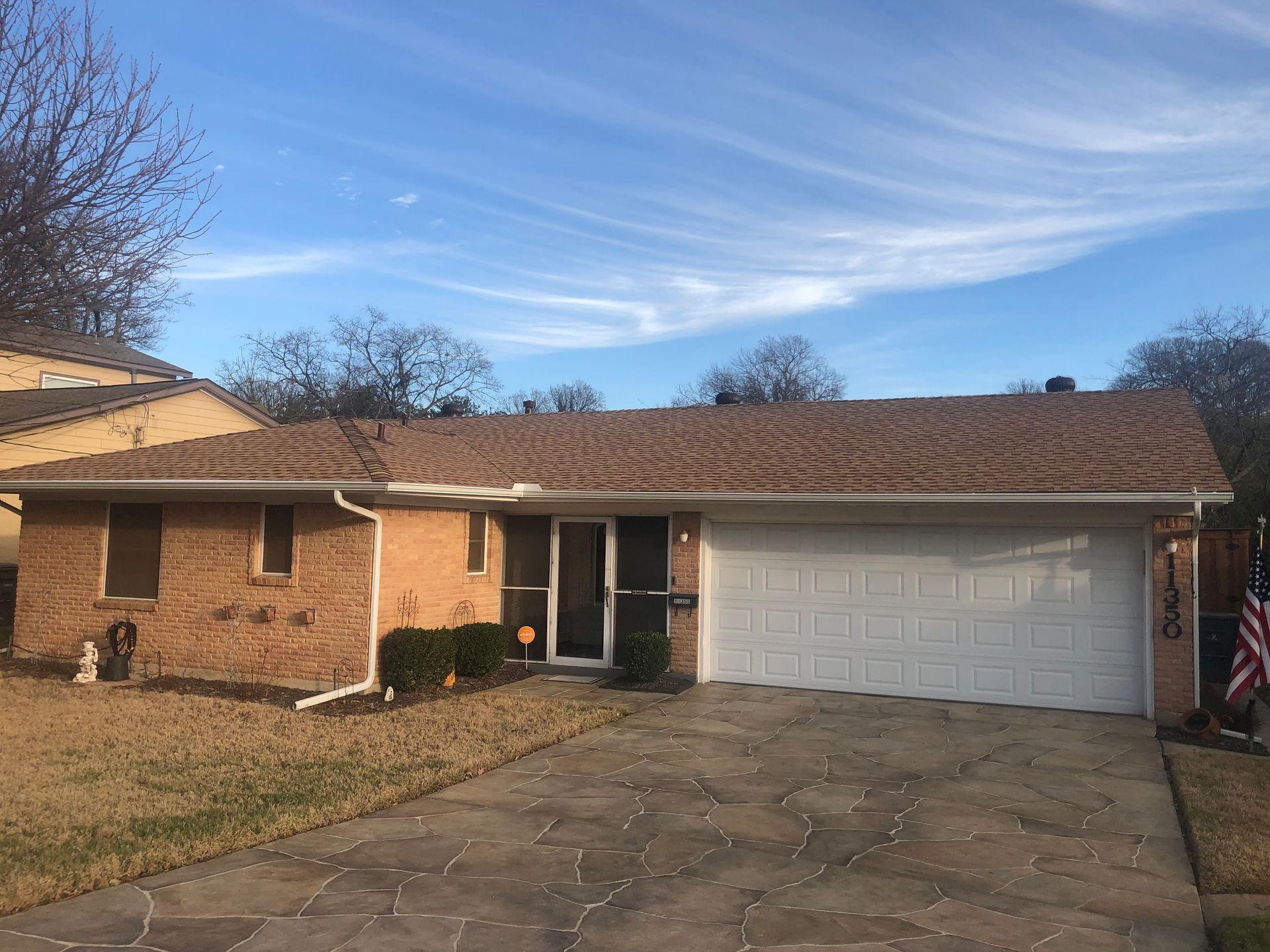 A brick house with a white garage door and an american flag in front of it.
