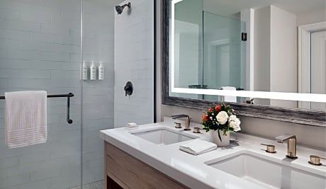 A bathroom with two sinks , a mirror and a walk in shower.