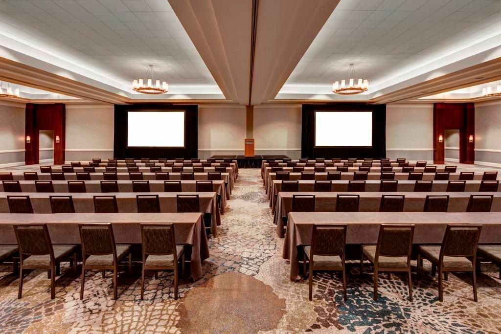 A large conference room with tables and chairs and two large screens.
