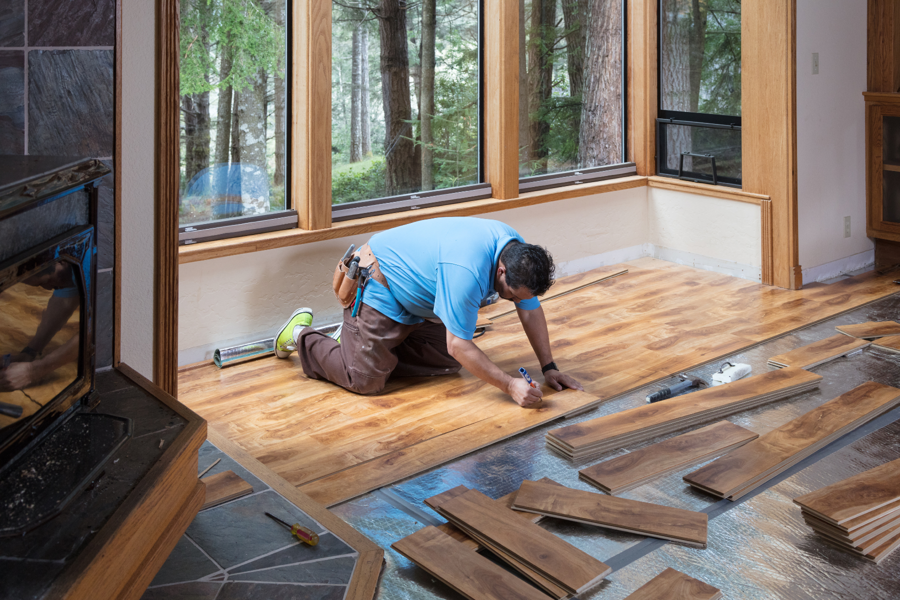 A man is installing a wooden floor in a living room.