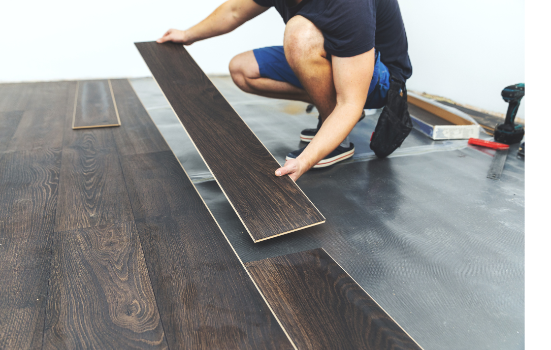 A man is kneeling down to install a wooden floor.