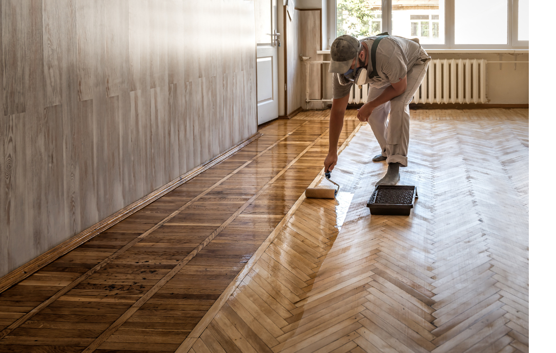 A man is painting a wooden floor with a roller.