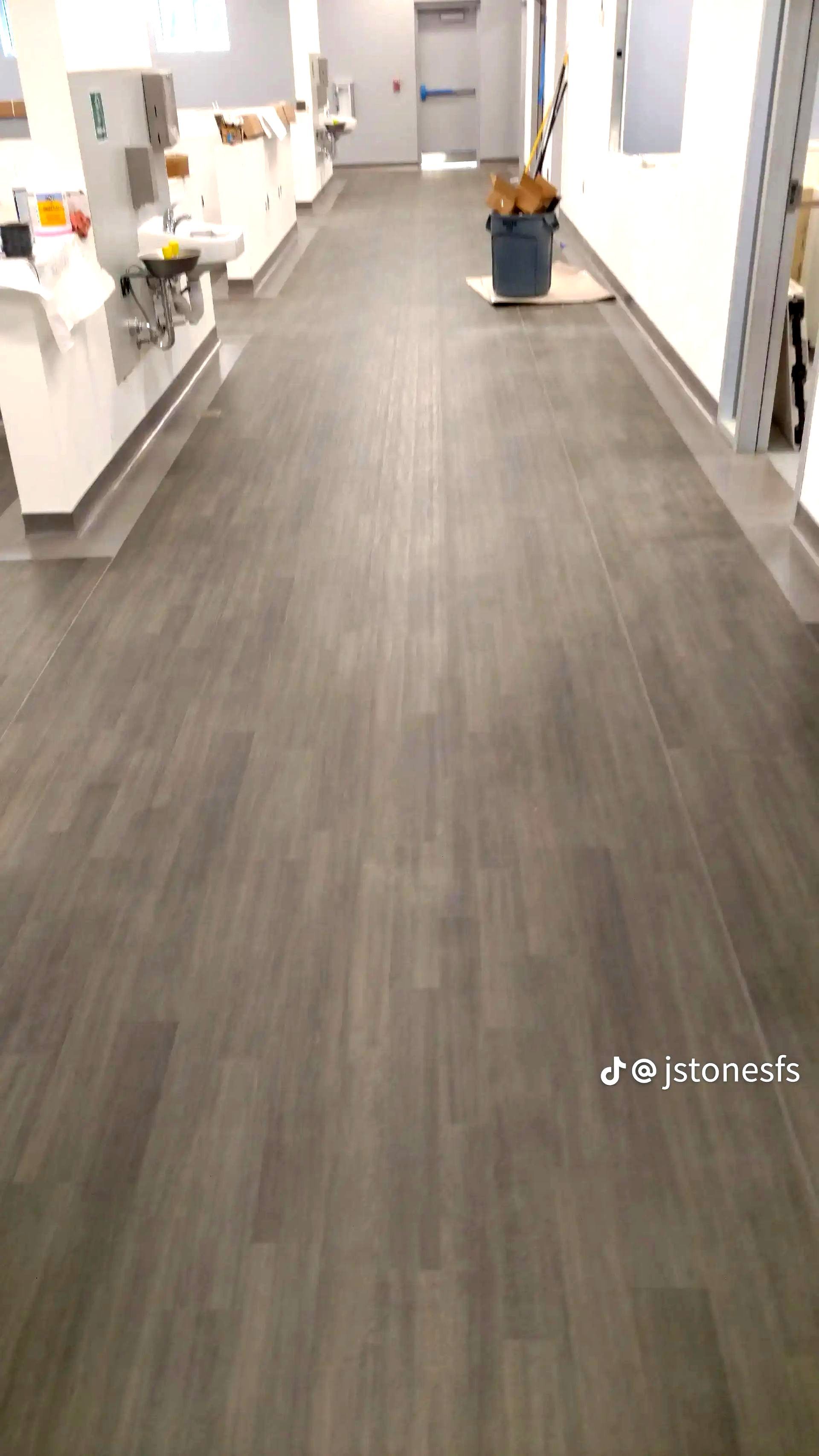 A long hallway with a wooden floor and a vase of flowers on the floor.