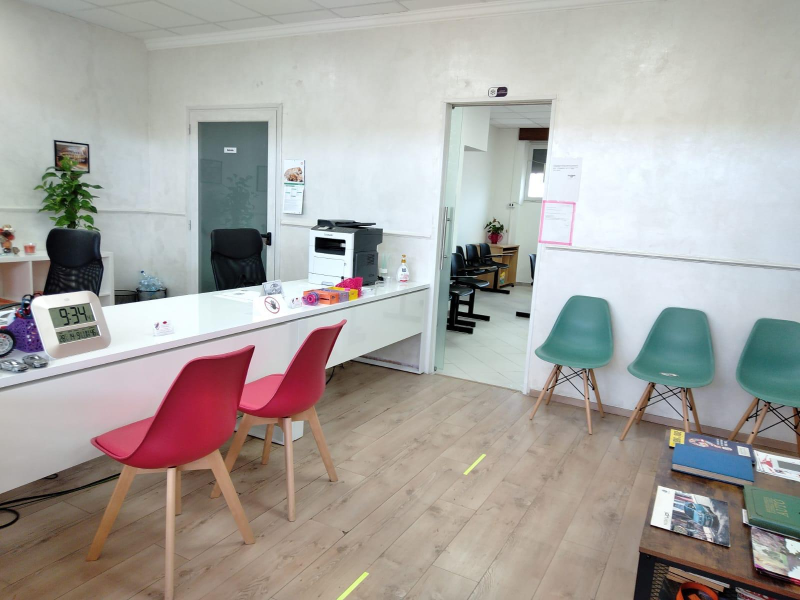 Area reception con scrivania bianca, sedie rosse e verdi e una porta che conduce alla palestra.