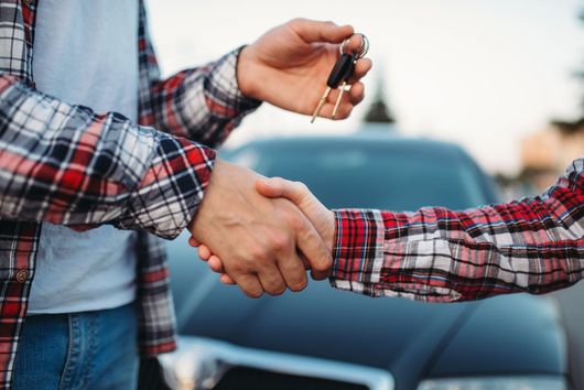 Persona che porge le chiavi dell'auto stringendo la mano davanti a un'auto.