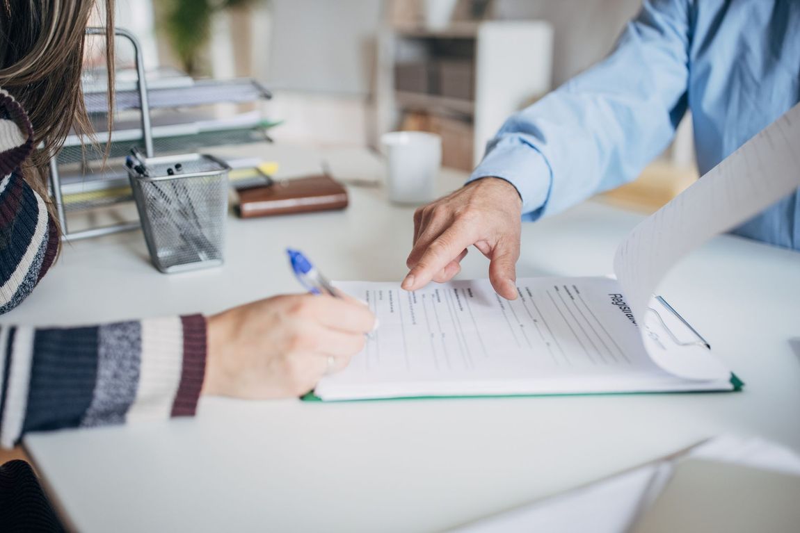 Persona che firma un documento alla scrivania mentre un'altra persona indica il testo.