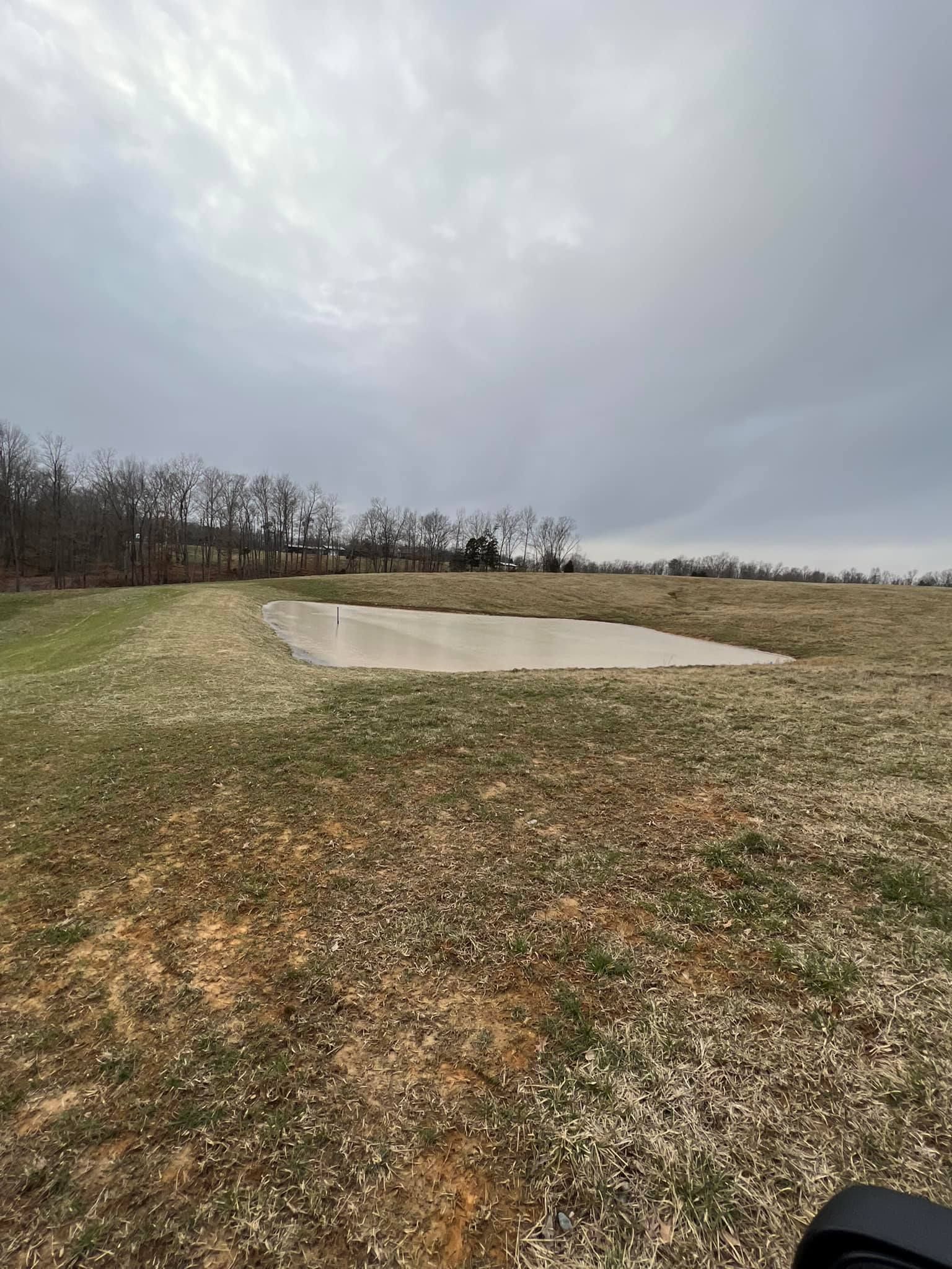 A construction site with a steep, gravel-covered slope leading up to a ridge of earth under a blue, cloudy sky.