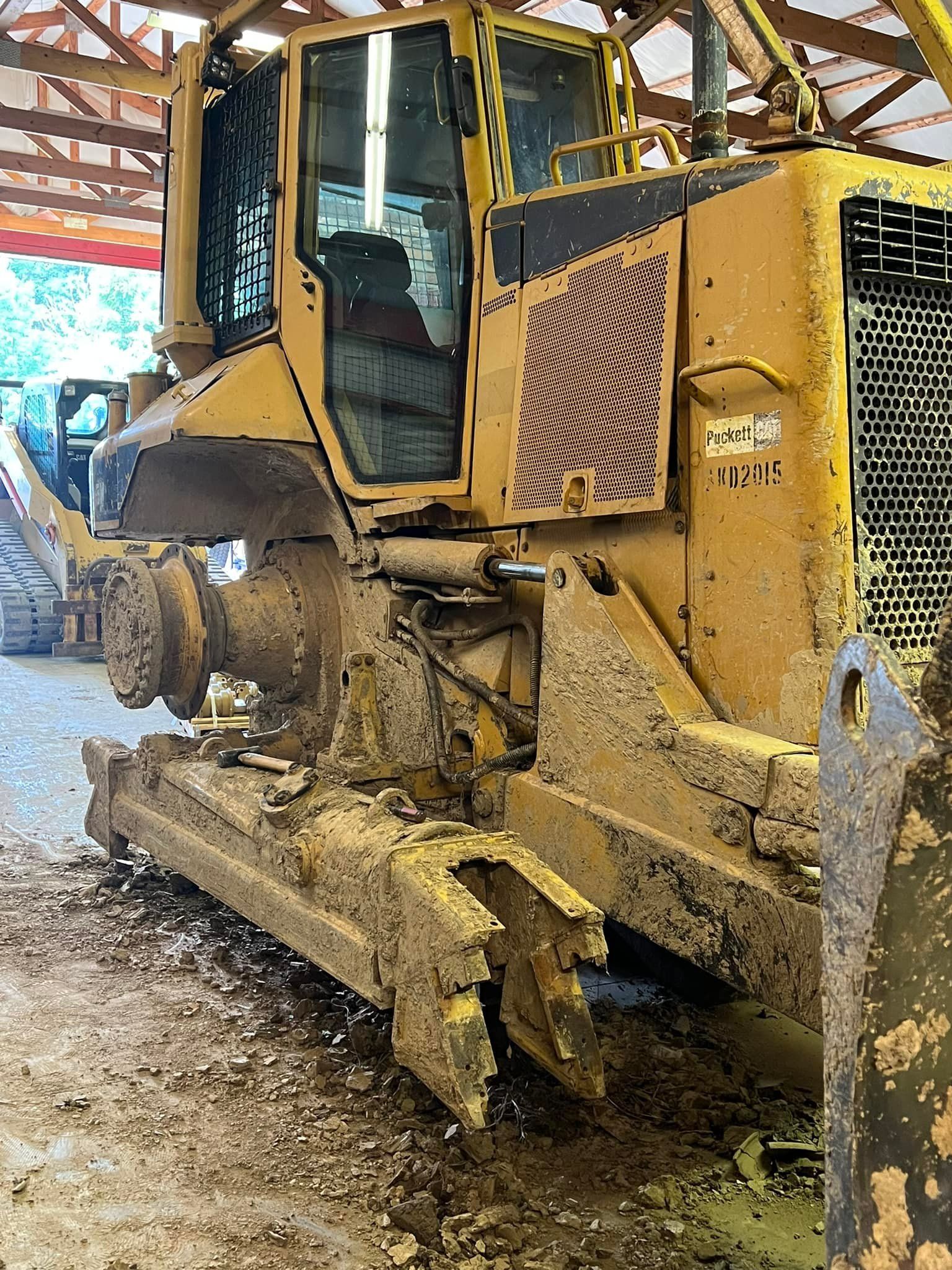A yellow bulldozer with missing tracks, parked in a covered outdoor area with a dirt floor.