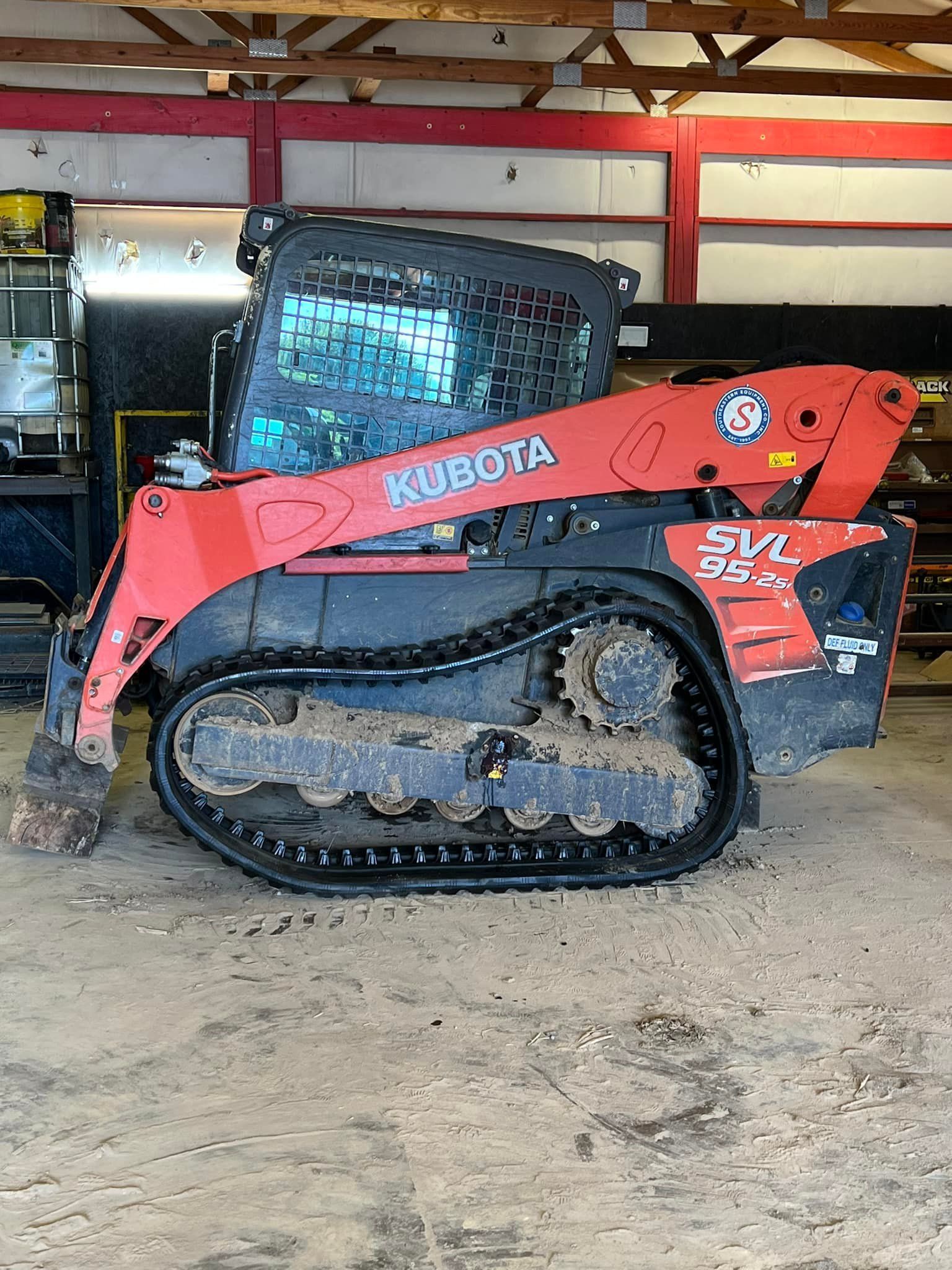 A bright orange Kubota SVL95 compact track loader parked inside a shop with a concrete floor.