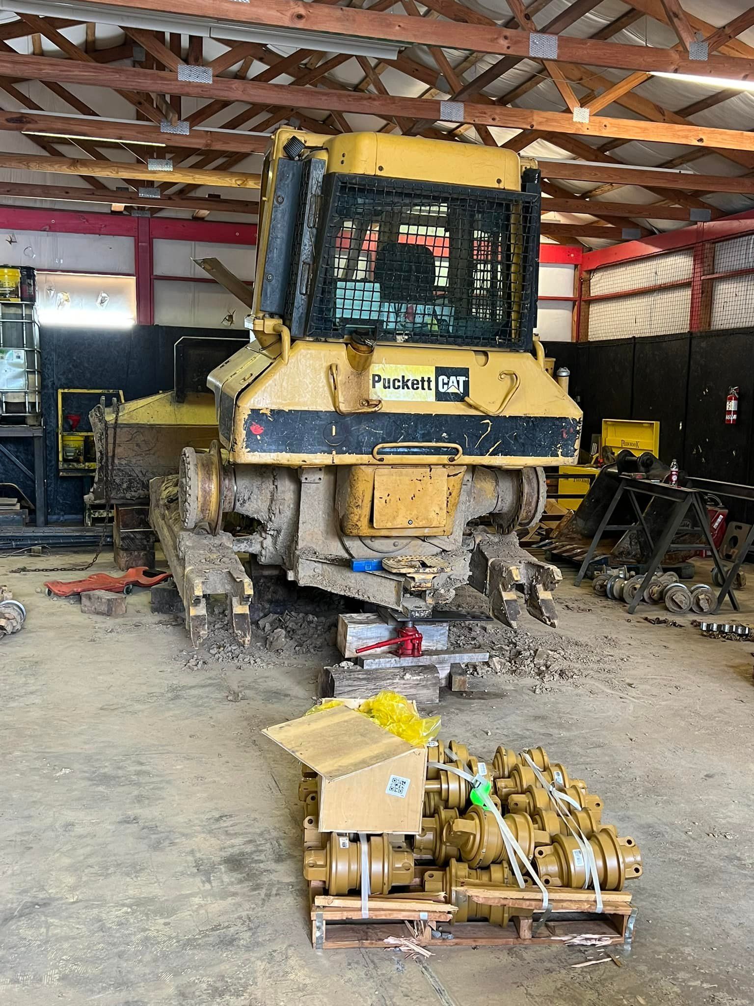 A yellow Caterpillar bulldozer undergoing maintenance inside a workshop, with tracks and new parts on a pallet nearby.