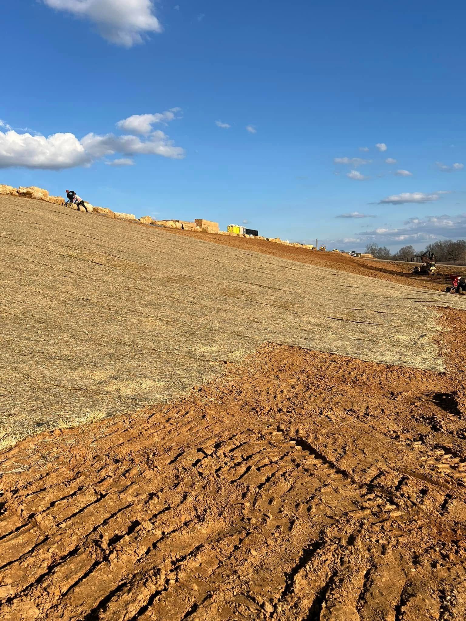 A sloped construction site showing a transition from loose, rocky soil on top to recently graded, brown dirt below.