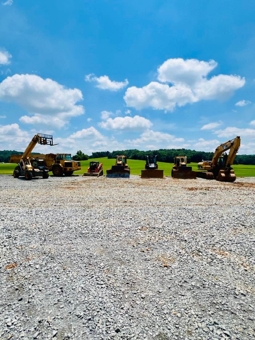 Construction equipment working on a large, cleared dirt lot surrounded by a treeline.
