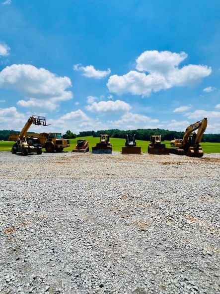 Construction equipment working on a large, cleared dirt lot surrounded by a treeline.