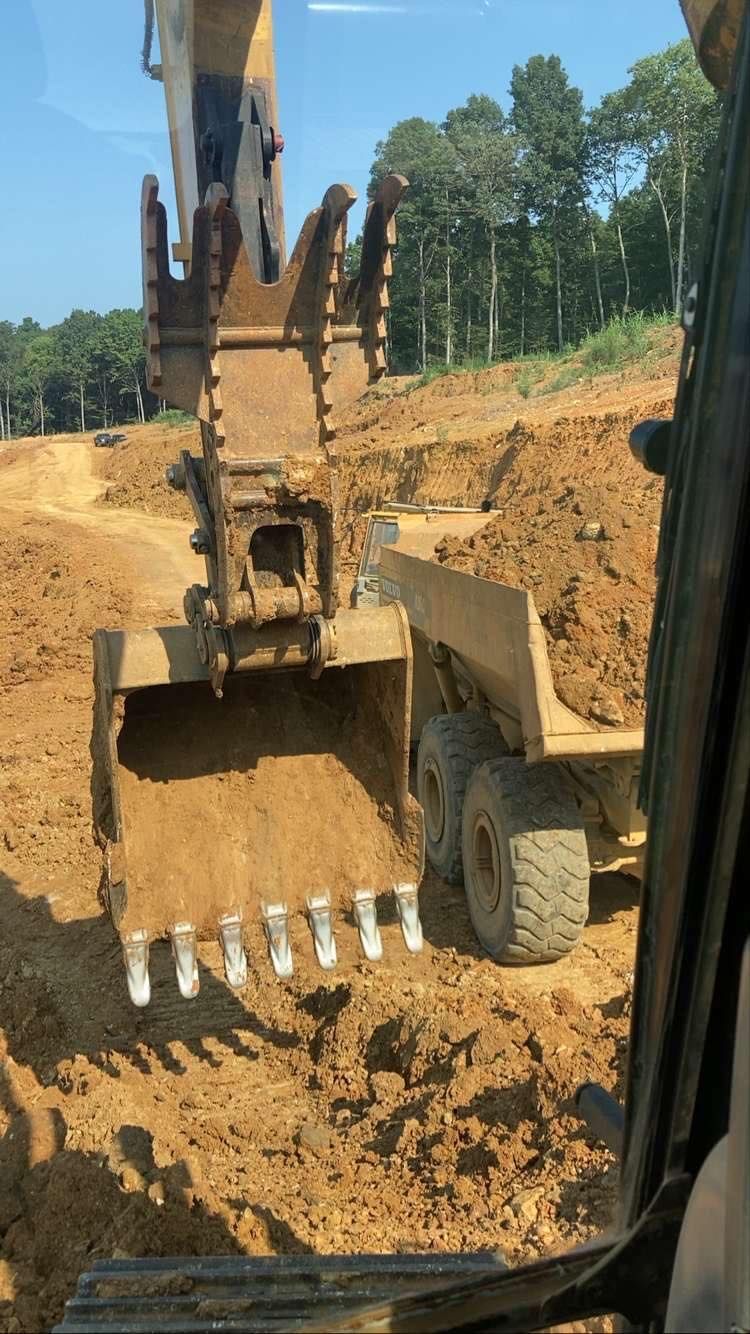 An excavator bucket loaded with dirt positioned over a dump truck at a construction site.