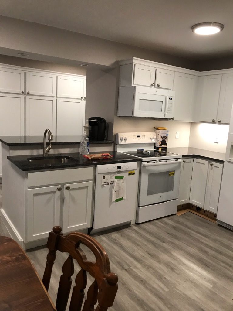 A kitchen with white cabinets , a stove , a sink , and a chair.