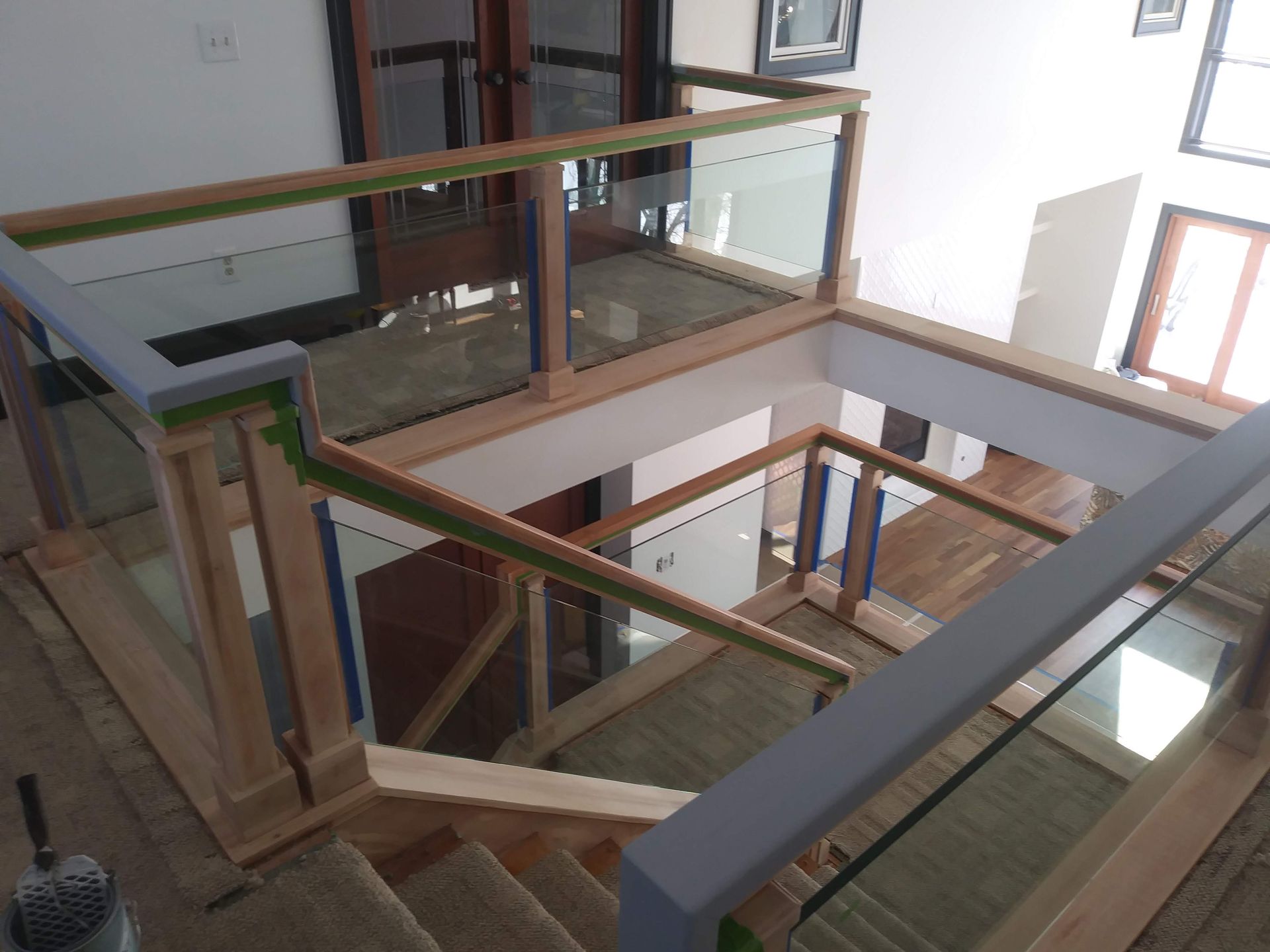 A wooden staircase with a glass railing is being built in a house.