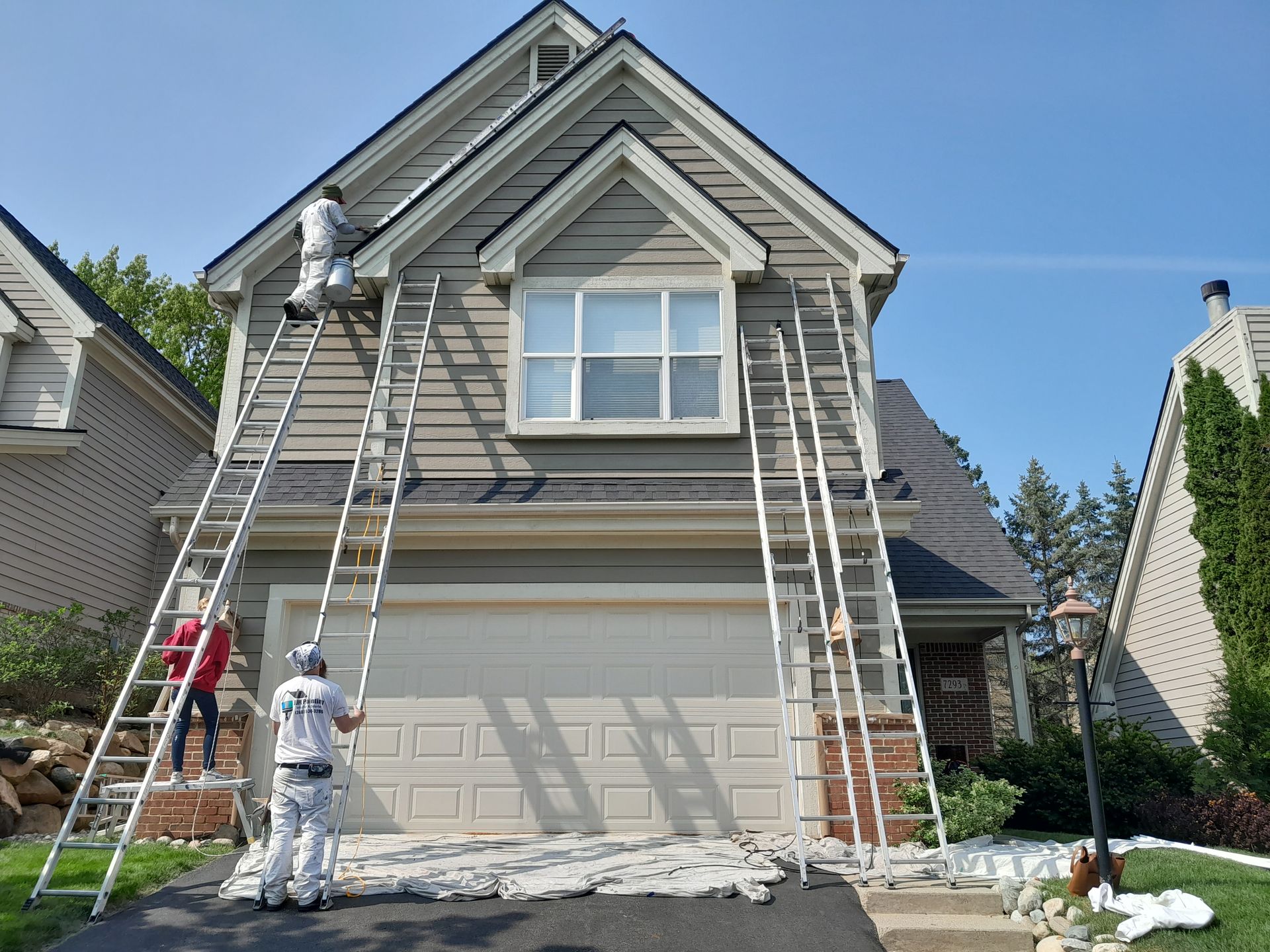 A group of people are painting a house with ladders.