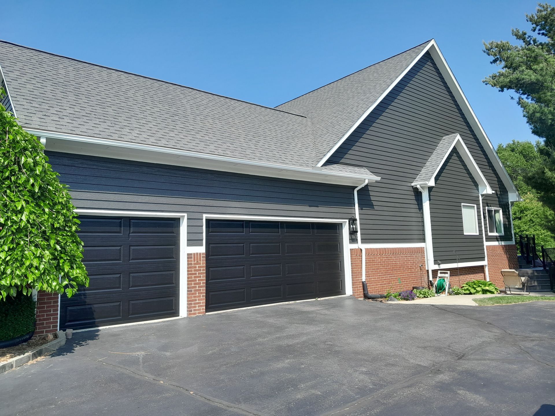 A large house with three black garage doors and a gray roof