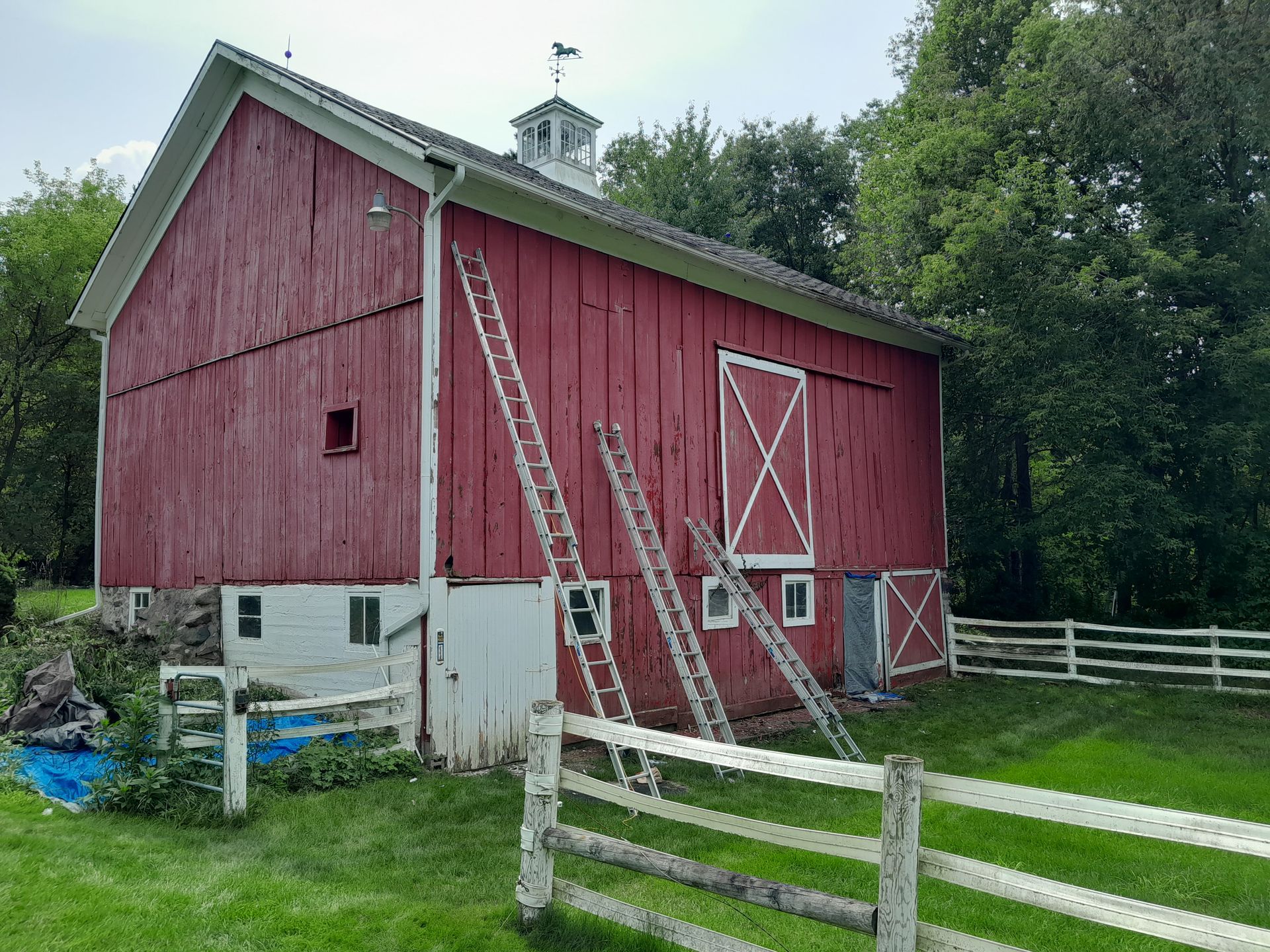 A red barn with a white fence in front of it is being painted.
