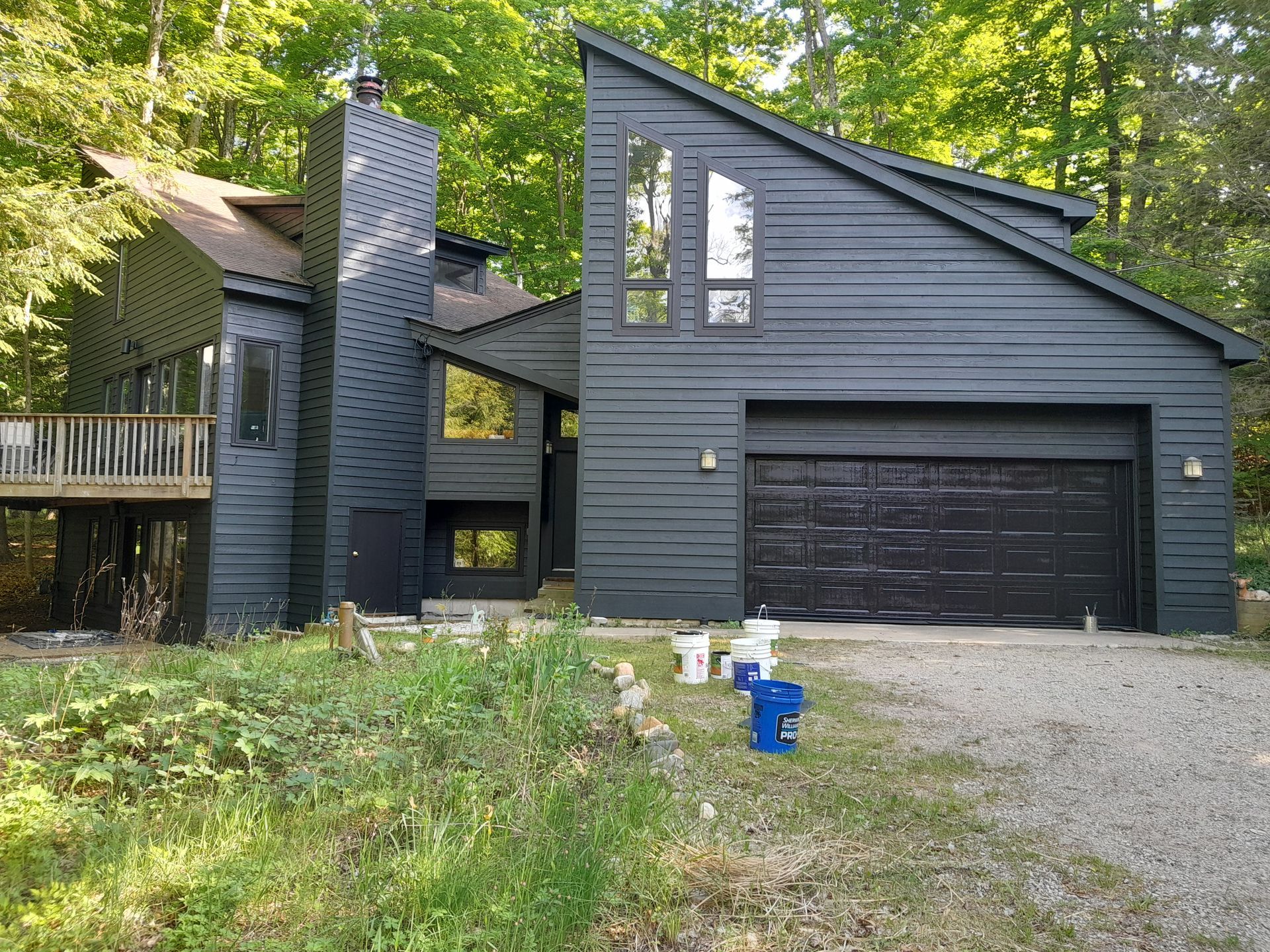 A black house with a black garage door is surrounded by trees.