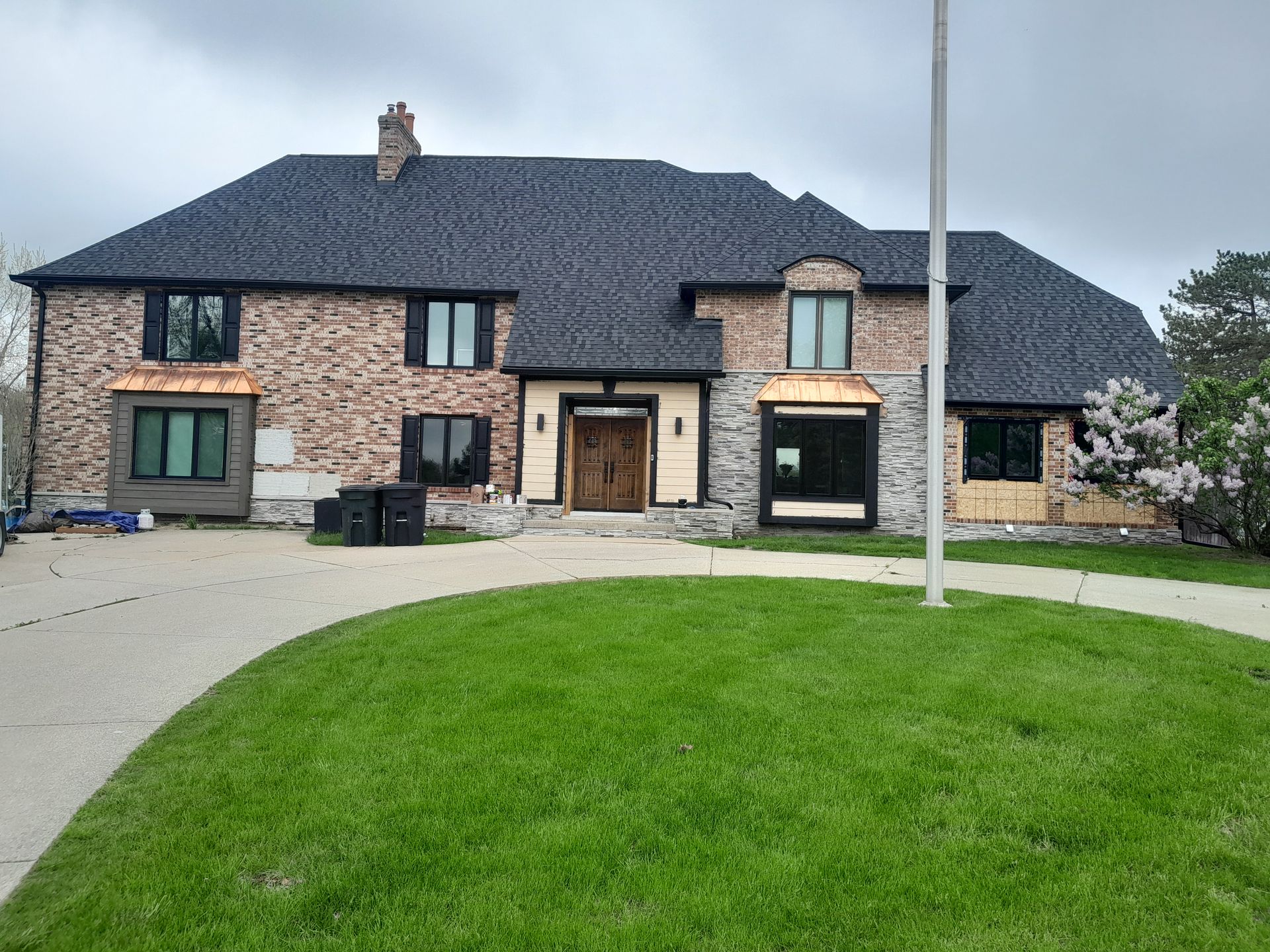 A large brick house with a black roof is sitting on top of a lush green lawn.