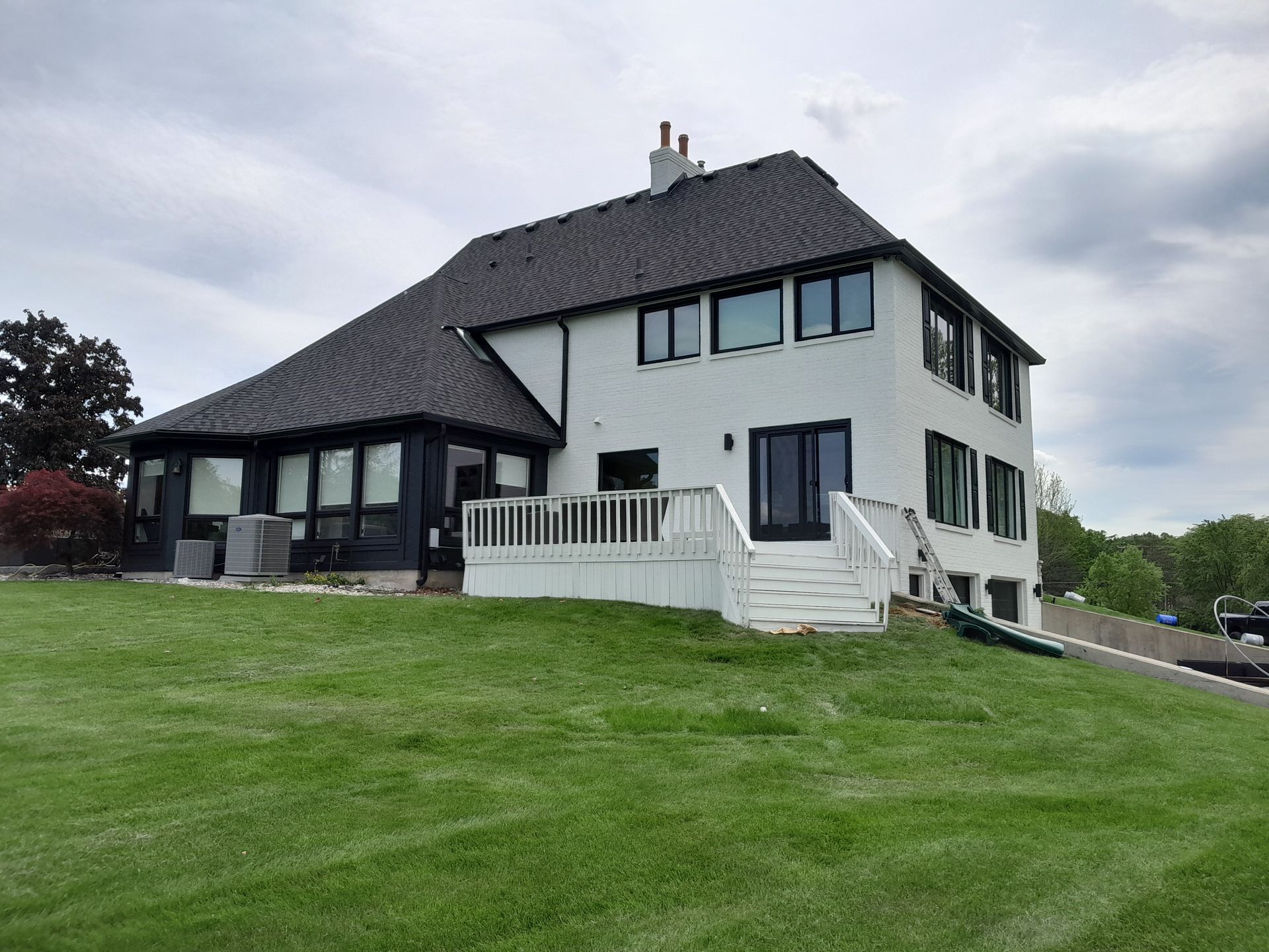 A large white house with a black roof is sitting on top of a lush green hill.
