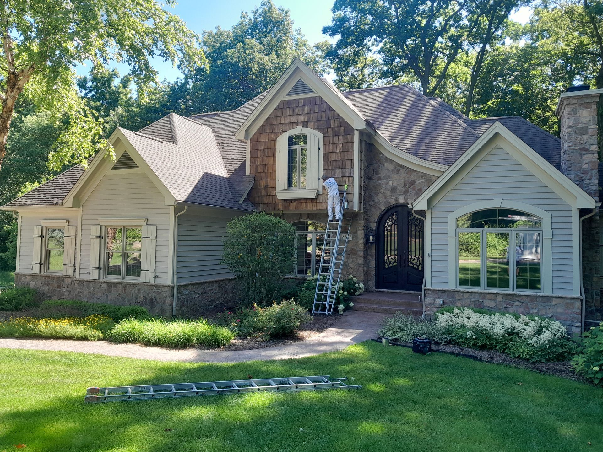 A man is standing on a ladder painting the side of a house.