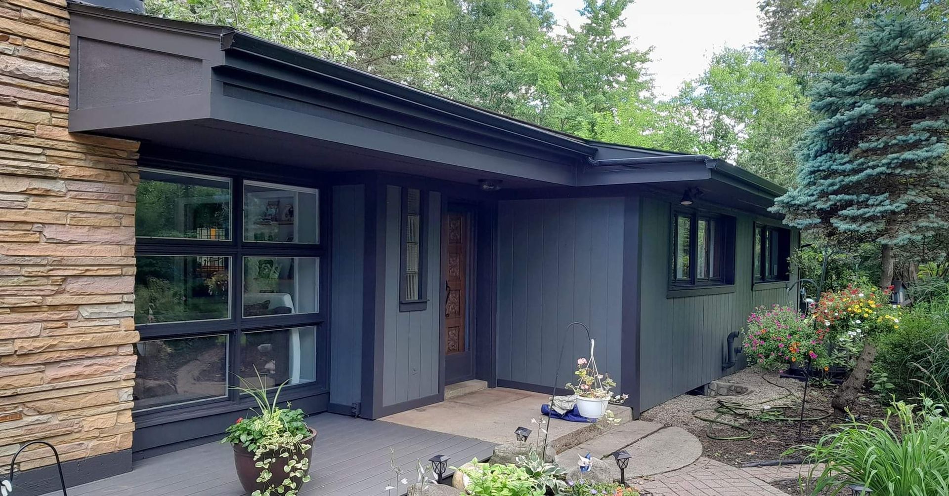 A house with a lot of windows and a stone wall is surrounded by trees.