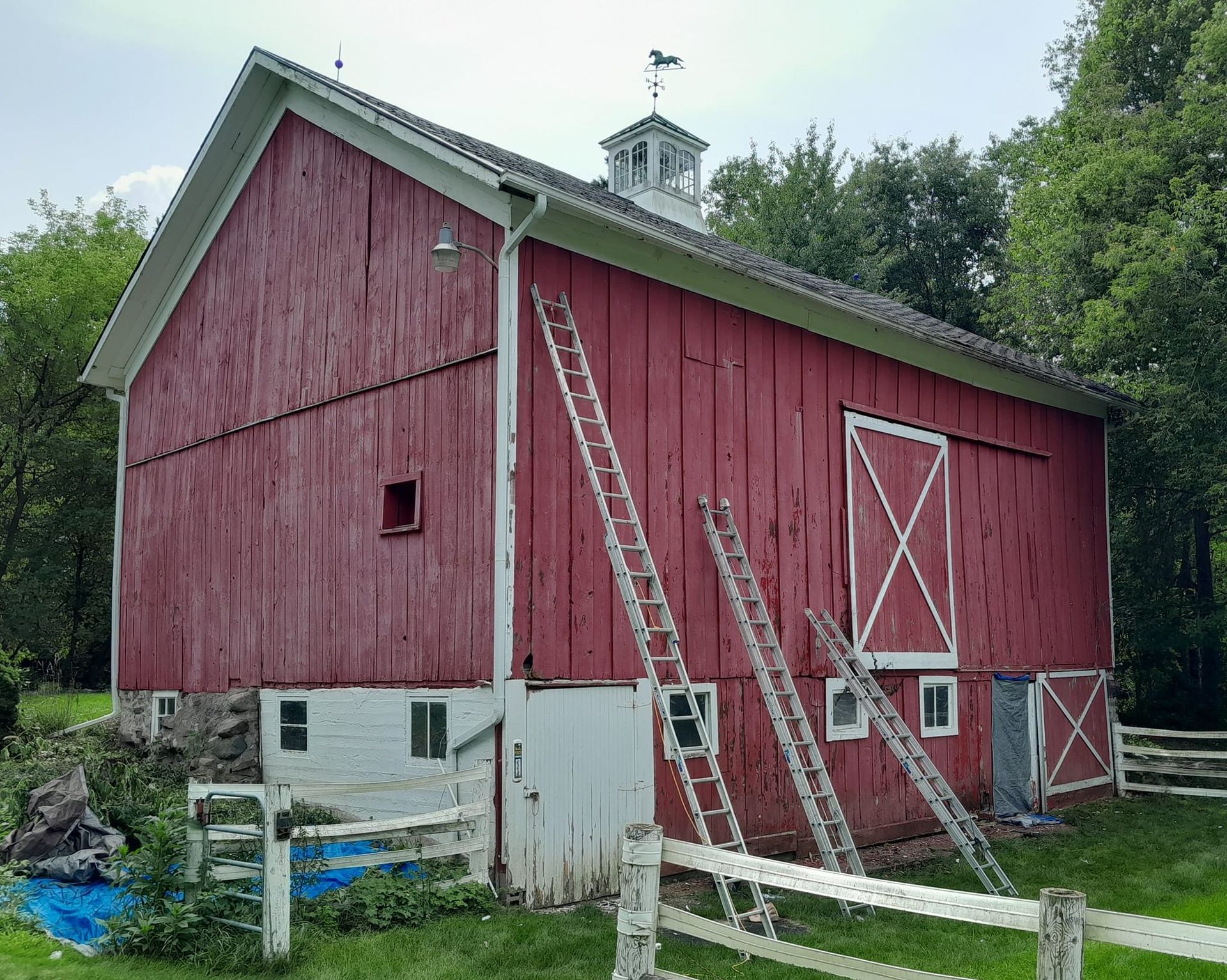 A red barn with a white door and a white fence in front of it.