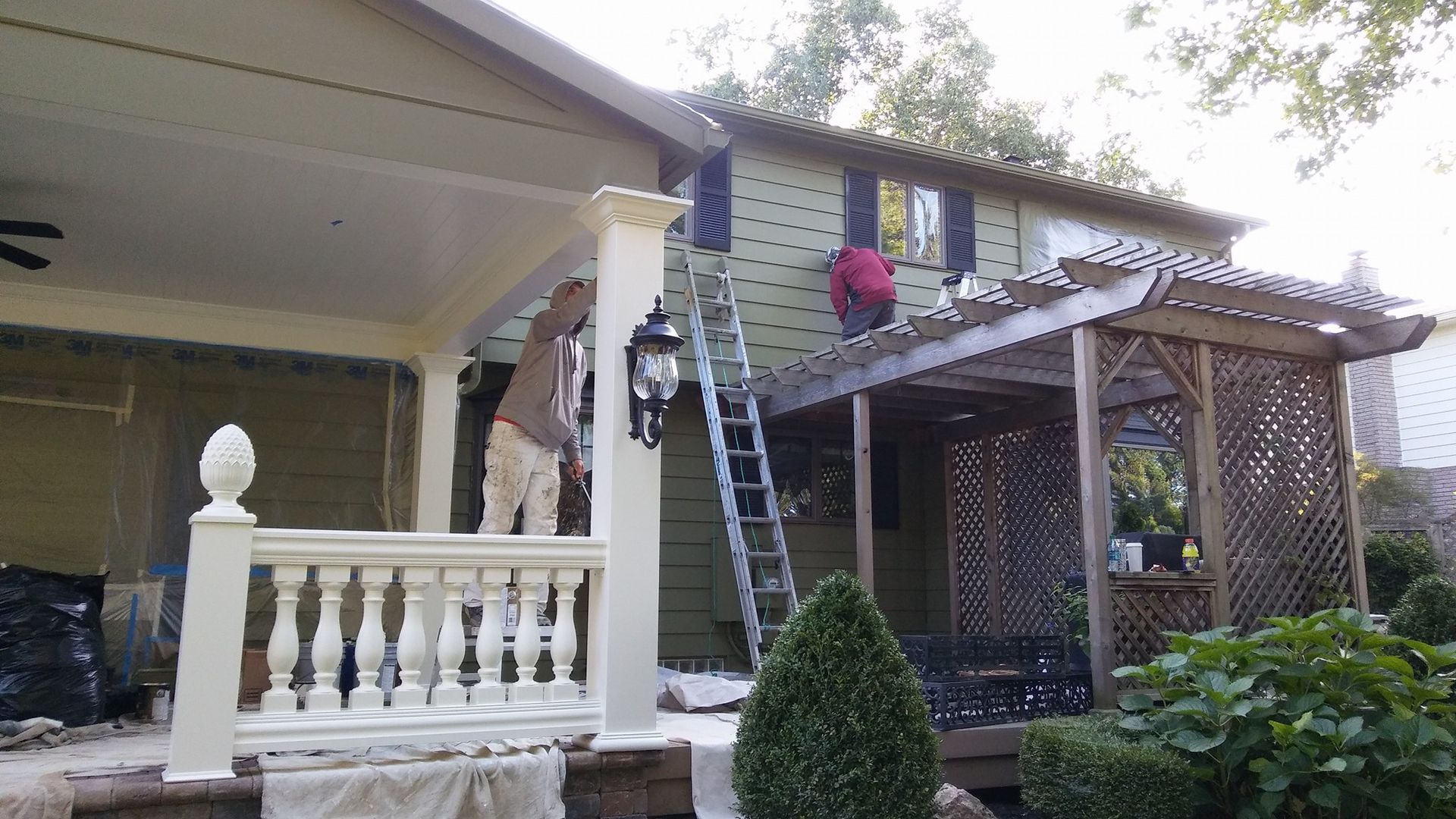 A man on a ladder is painting the side of a house.