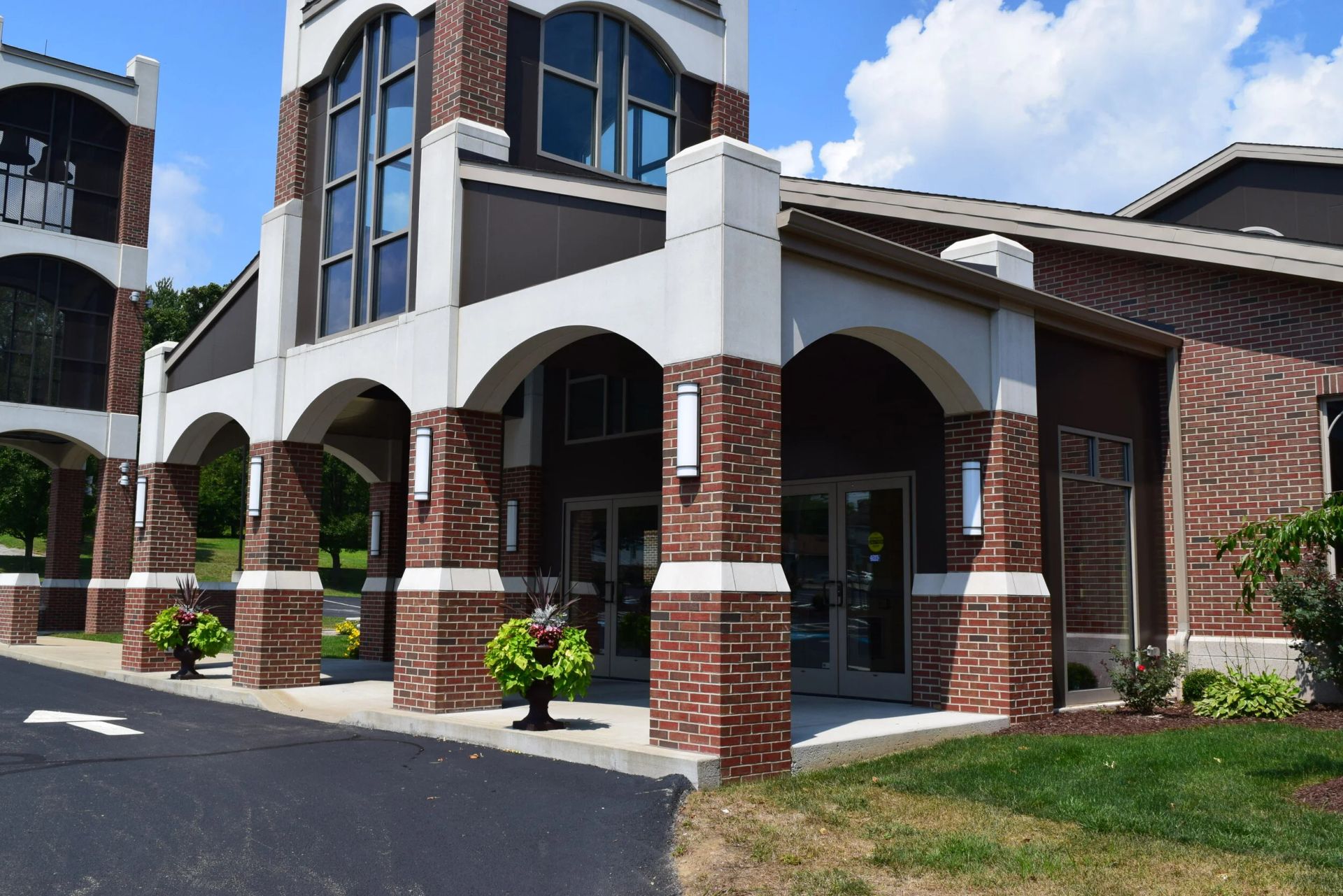 Brick apartment building with white arches and blue windows along a paved driveway under a partly cloudy sky