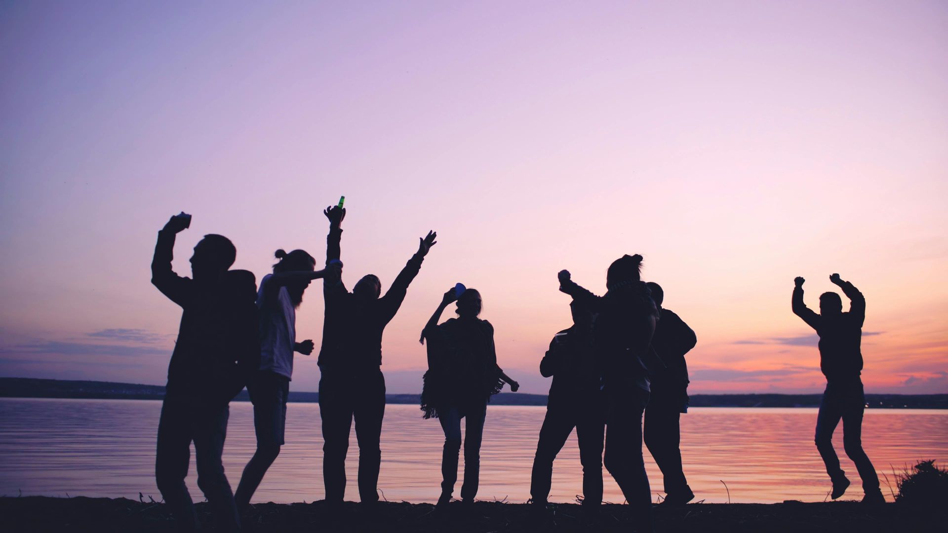 Silhouetted group dancing and posing on a beach at sunset with pink and orange sky