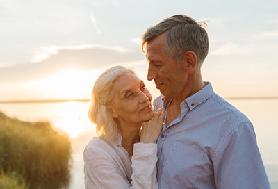 an elderly couple is hugging each other on the beach at sunset .
