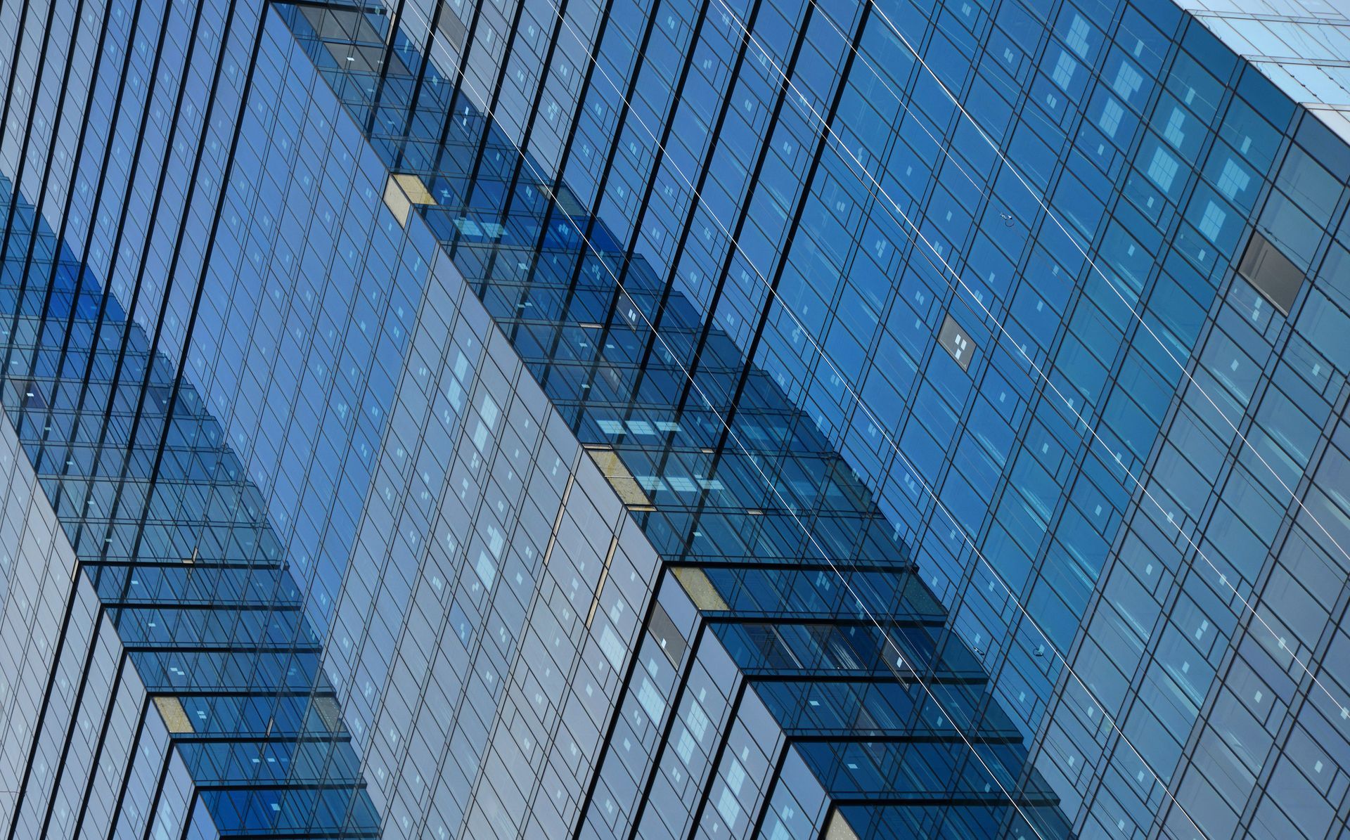 Blue glass skyscraper, angled view, reflecting light, with grid pattern windows.