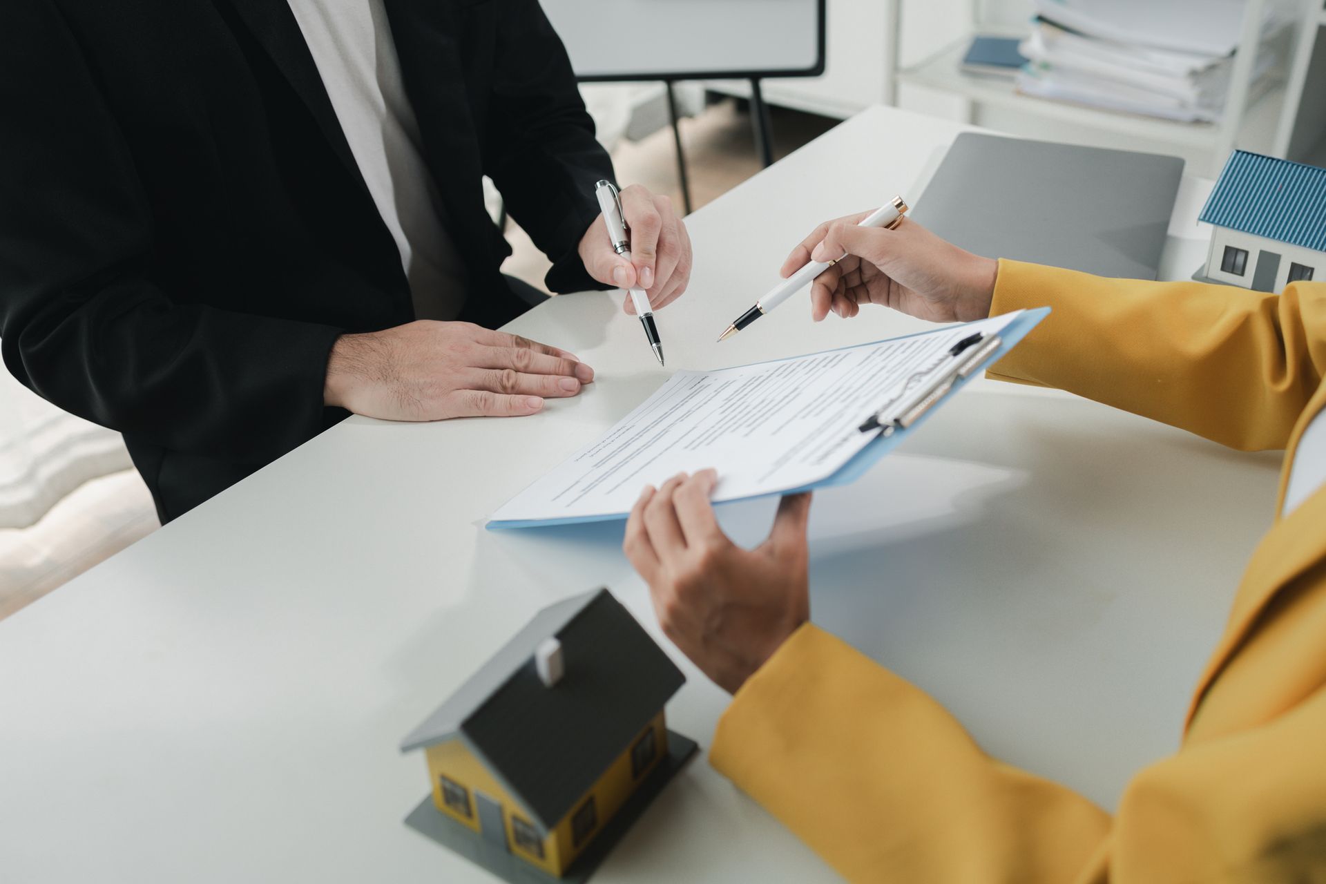 Two people signing documents at a desk, toy houses present.