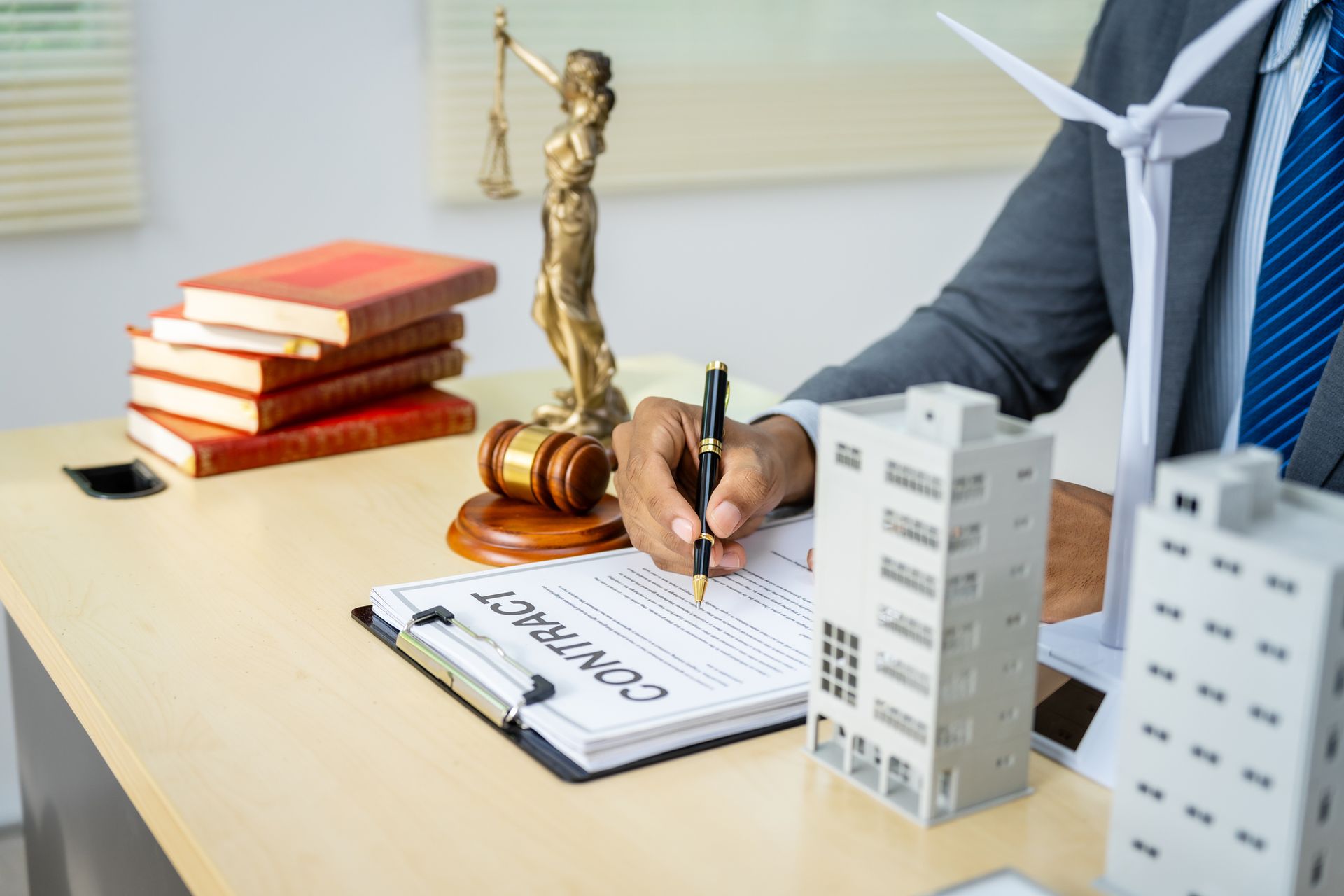Person in suit with hands over a toy house; coins and paperwork on a desk.