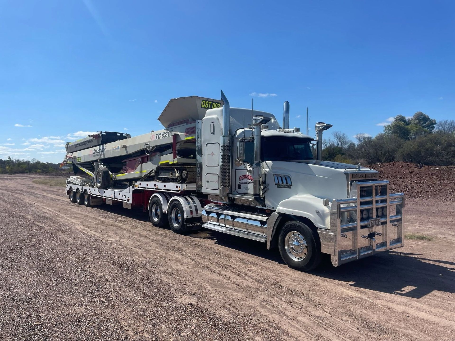 White Semi-Truck Hauling a Large Boat on A Trailer Along a Dirt Road — Rainbow and Sons Heavy Haulage in Wells Crossing, NSW