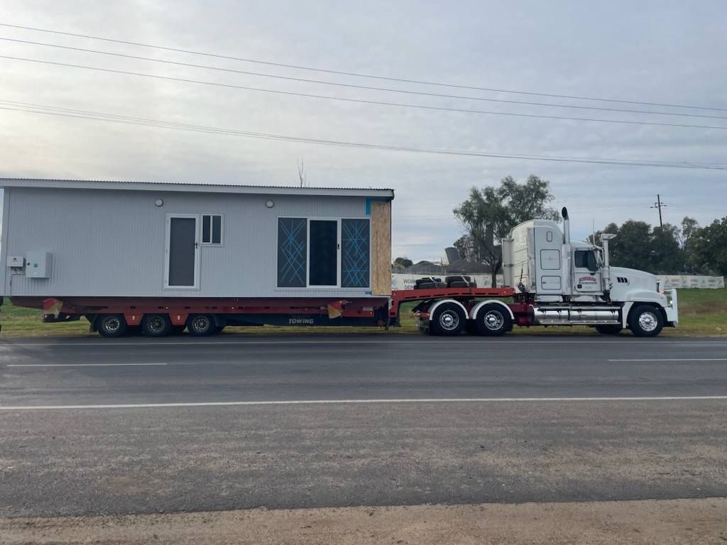 White Semi Truck Hauling a Gray Modular Home on A Highway — Rainbow and Sons Heavy Haulage in Wells Crossing, NSW