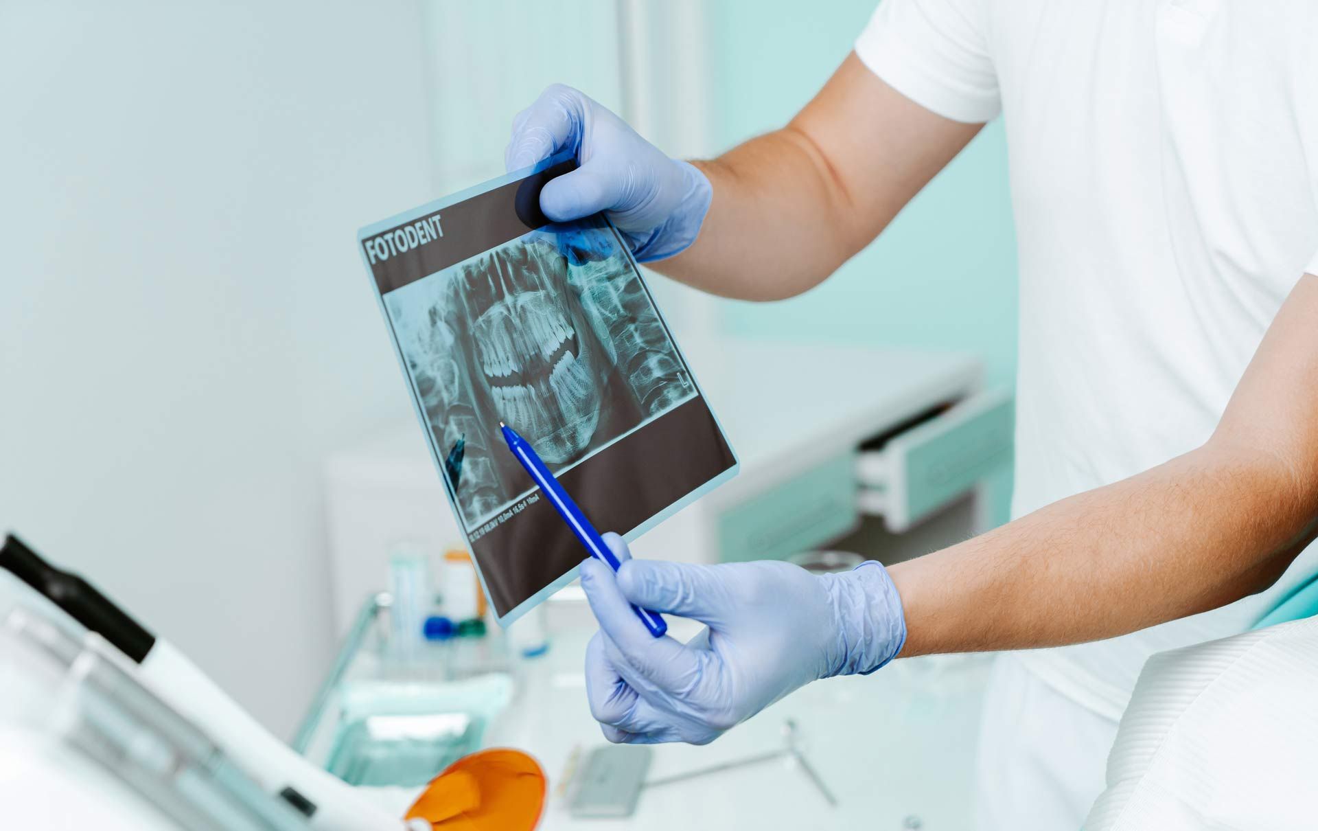 Doctor in blue gloves reviewing an X-ray and pointing with a pen in a clinic