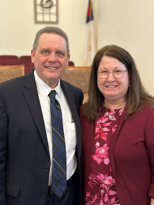 Man in suit and woman in floral dress smile together indoors.