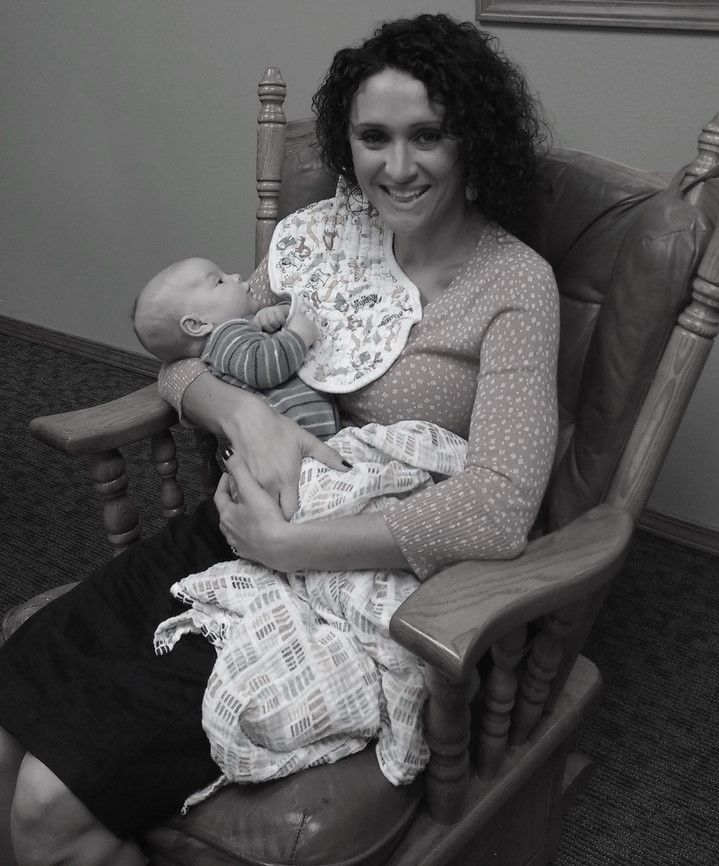 Woman smiling, holding baby in a rocking chair, with a bib and blanket.