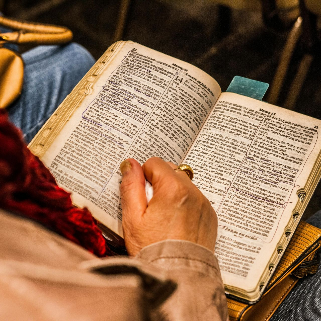 Person holding open, well-worn book, reading with a finger marking a page, indoors.