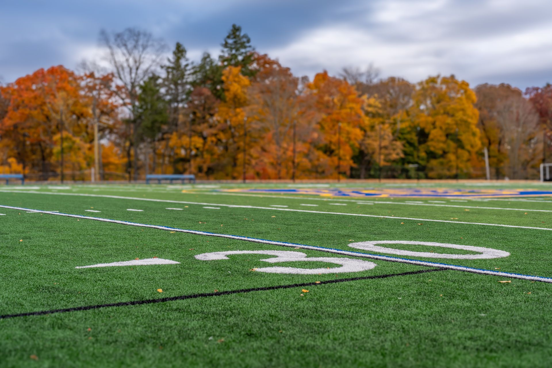 Football field, 30-yard line in focus, autumn trees in background with vibrant orange leaves.