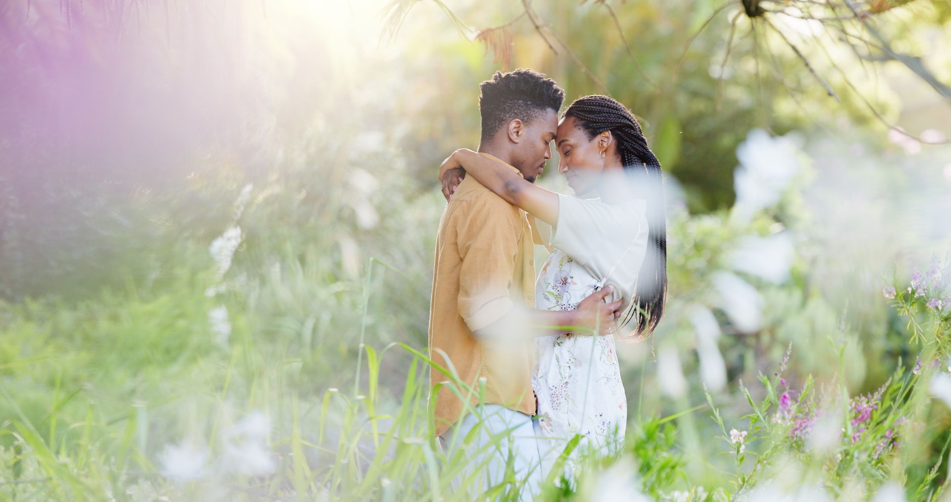 Couple embracing in a field of wildflowers; sunlight streams through the trees.