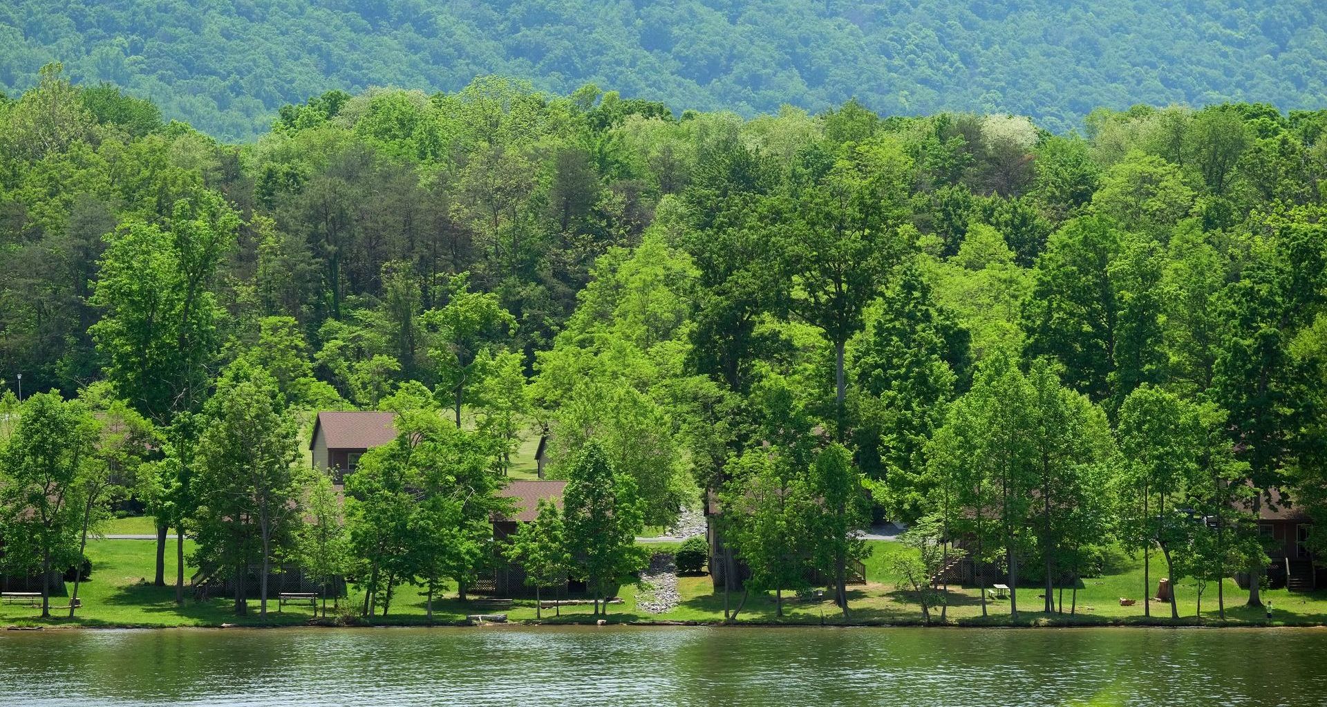 A lake surrounded by trees and mountains with a house in the background.